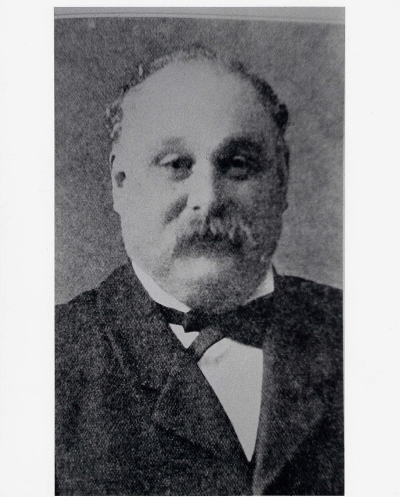 Portrait officiel en noir et blanc d’un homme au crâne dégarni portant une moustache.