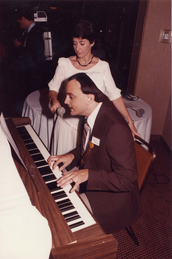 Homme au piano et femme debout à côté de lui, tenant un micro.