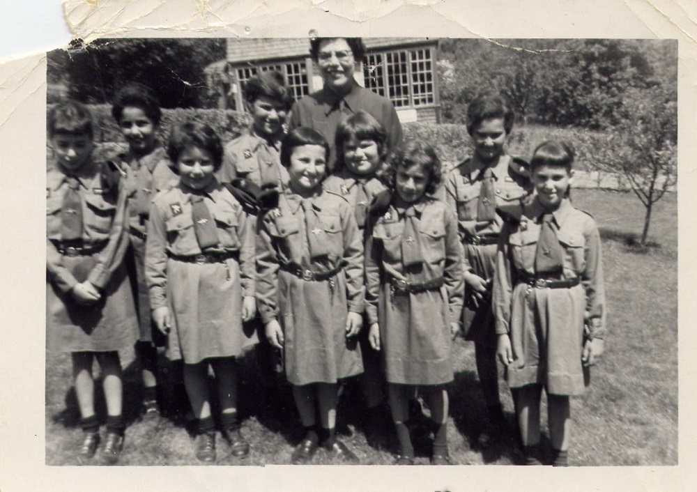 Neuf fillettes en tenue de jeannette avec leur chef également en uniforme en arrière-plan.