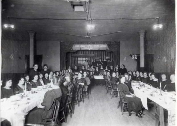 Femmes assises à de longues tables et table d’honneur à l’arrière-plan.