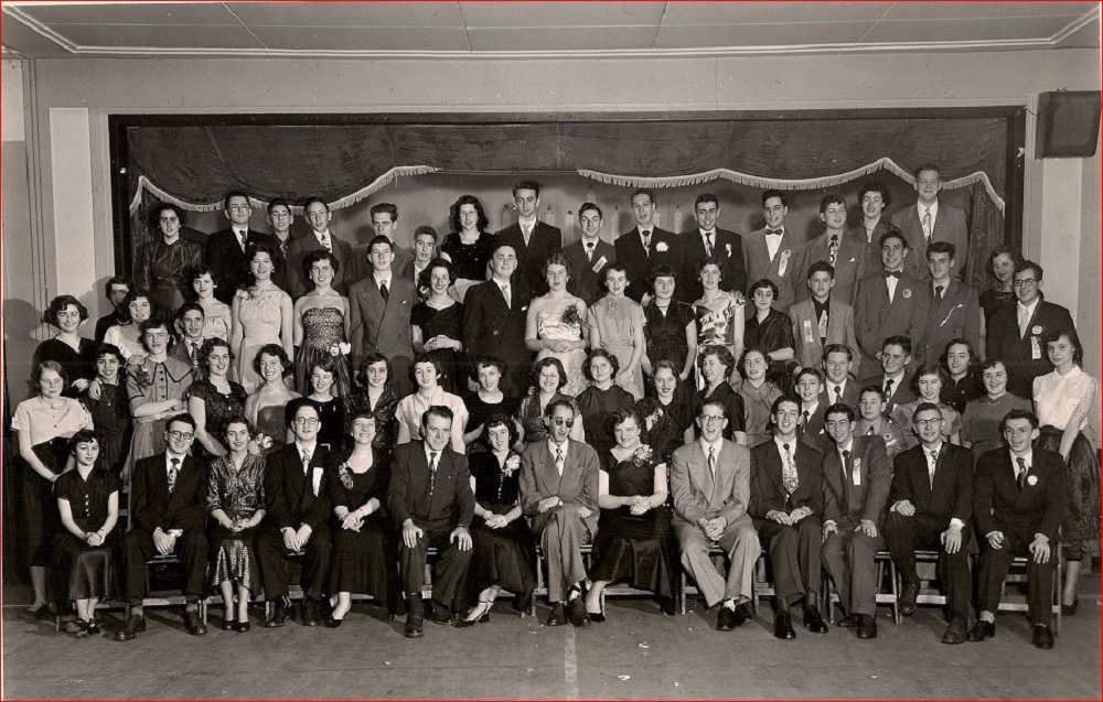 Soixante-dix jeunes hommes et femmes en tenue de soirée disposés en quatre rangées.
