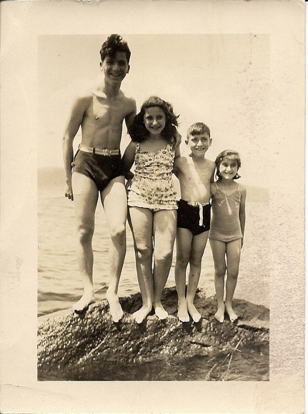 Quatre enfants en maillot de bain juchés sur un rocher. De gauche à droite, ils se tiennent du plus grand et plus âgé à la plus petite et plus jeune.