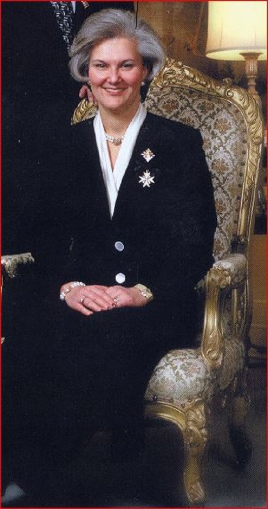 Portrait officiel d’une femme aux cheveux grisonnants portant un tailleur à jupe longue et posant assise dans un fauteuil richement décoré.