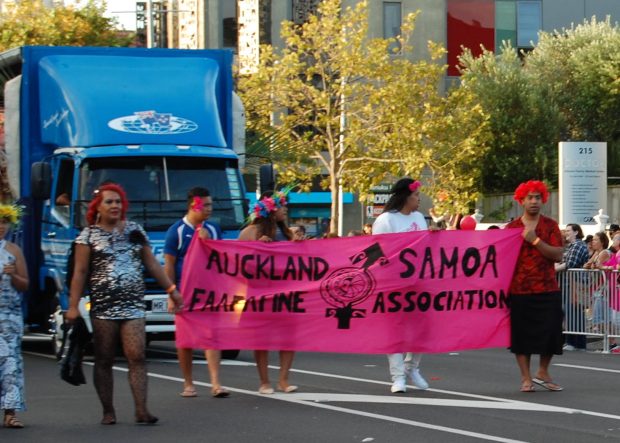 Cinq personnes tenant une bannière lors d’un défilé de rue. La bannière indique AUCKLAND SAMOA FAAFAFINE ASSOCIATION.