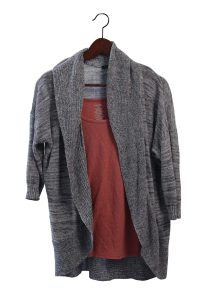 Un cardigan gris sur un haut rose, sur un cintre en bois.