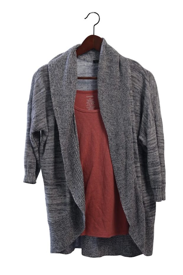 Un cardigan gris sur un haut rose, sur un cintre en bois.