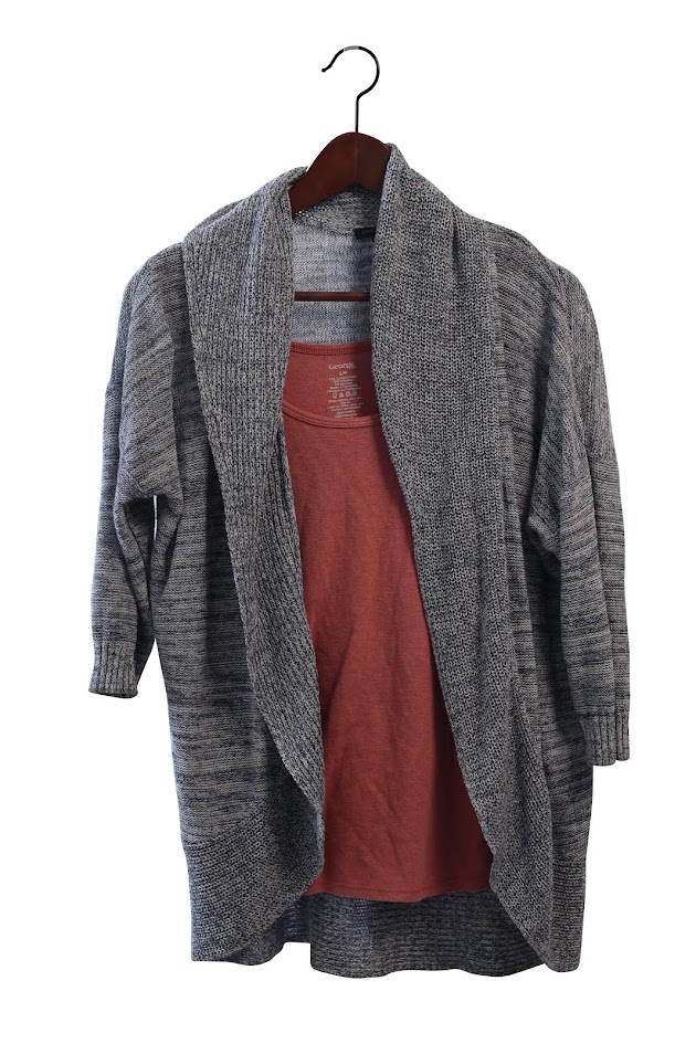 Un cardigan gris sur un haut rose, sur un cintre en bois.