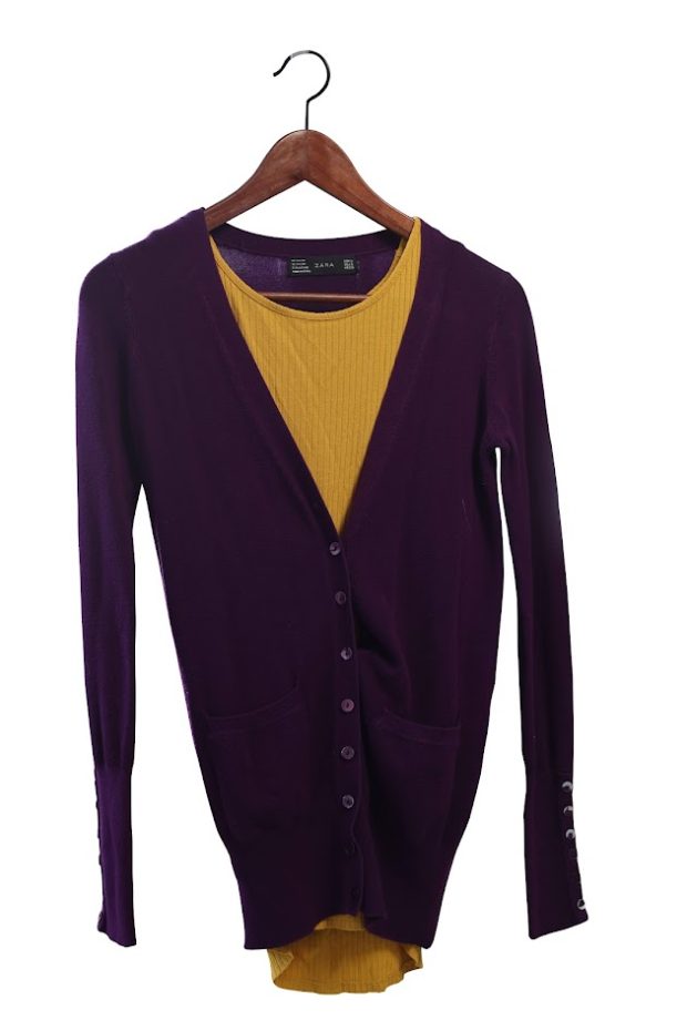 Un cardigan pourpre, boutonné, sur un haut jaune, sur un cintre en bois.