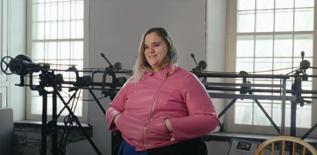 Une personne vêtue d’une veste rose vif debout devant une machine à coudre sur rails.