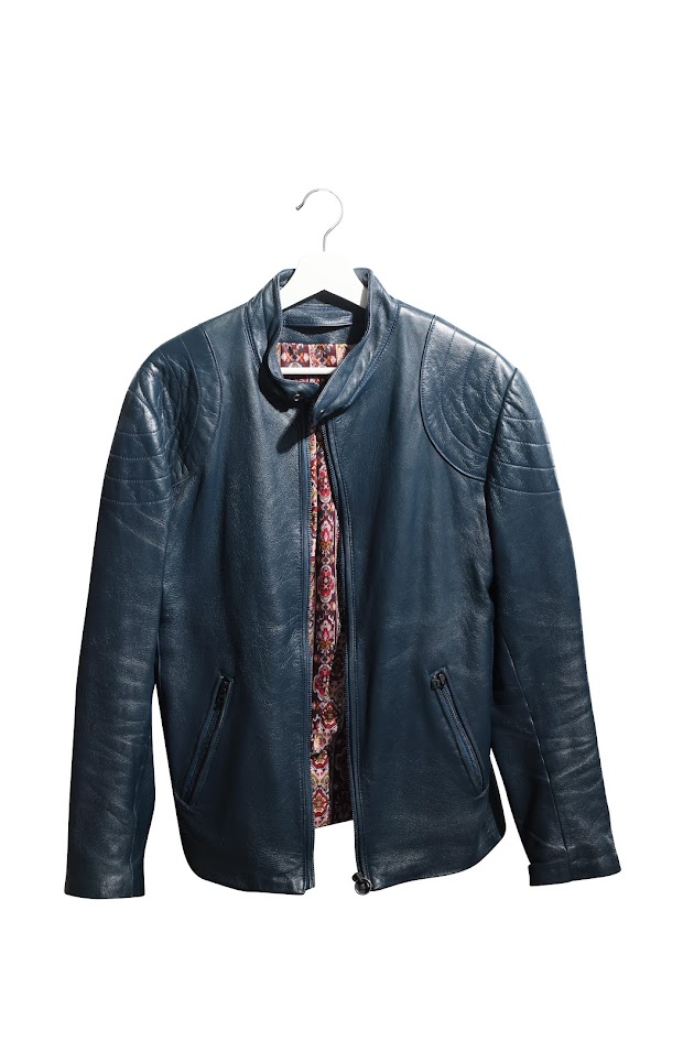Une veste en cuir bleu foncé sur un cintre blanc. La veste est légèrement ouverte, révélant une doublure colorée.