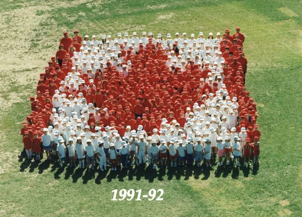 Photo en couleur vue d’en haut montrant un groupe d’élèves habillés en rouge ou en blanc debout sur l’herbe et formant un drapeau canadien.