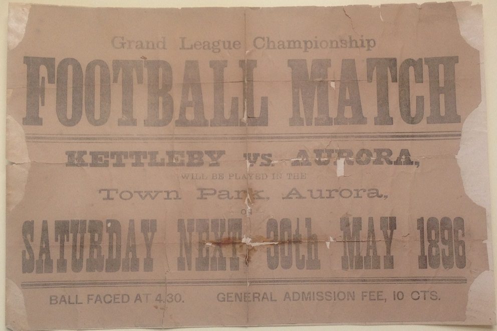 Affiche horizontale sur fond brun annonçant un match de foot dans le parc municipal. Trois côtés sont déchirés.