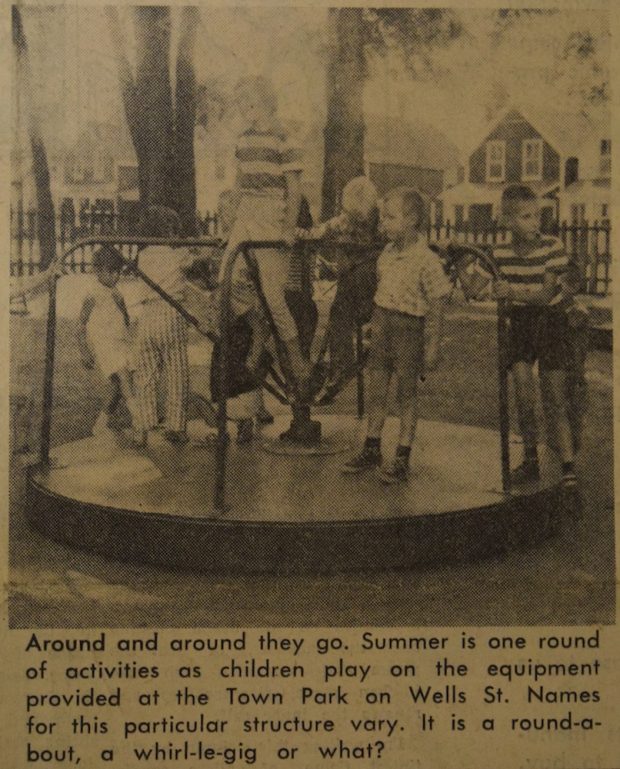 Image sépia, noire et grise de neuf enfants  sur un manège dans un parc.  A l’arrière une clôture en bois et des maisons.  Il y a une petite légende en noir sous l’image.