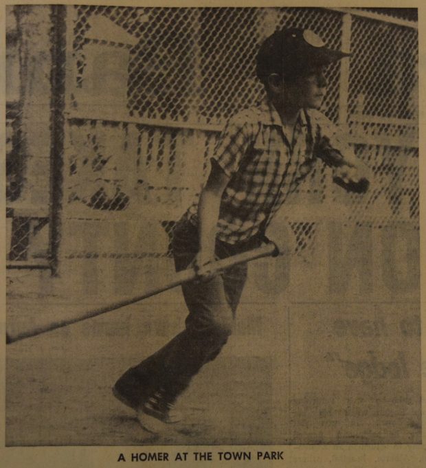 Image en sépia et noir d’un jeune garçon jouant au baseball.  Il tient une batte juste après avoir frappé une balle.  Il regarde au loin et on dirait qu’il s’apprête à courir.  On voit une clôture métallique à l’arrière et une petite clôture en bois.  Courte légende en noir sous l’image.