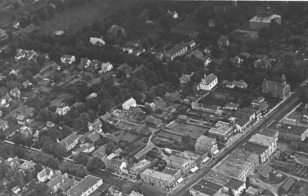 Une image aérienne en noir et blanc montre six pâtés de maison.  On y voit plusieurs bâtiments publics et résidentiels ainsi qu’un parc dans le coin supérieur gauche.