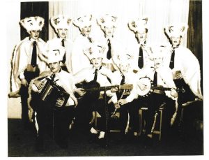 La photographie en noir et blanc montre un groupe de musiciens costumés à l’occasion de la Mi-Carême.