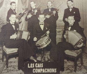 Photographie promotionnelle en noir et blanc des Gais compagnons devant un faux décor. Les membres sont vêtus de complets et de nœuds papillon.