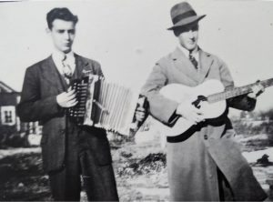 Photographie en noir et blanc d'Armand Labrecque, à droite, un accordéon à la main. Monsieur Casault à la guitare lors d’un rassemblement familial.