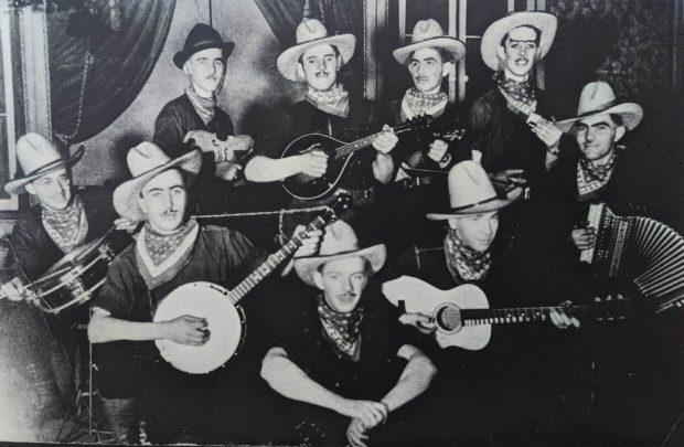 La photographie promotionnelle en noir et blanc montre l’orchestre Montminy. Les musiciens ont tous un chapeau de cowboy et un foulard au cou. Derrière eux se trouve un faux décor.
