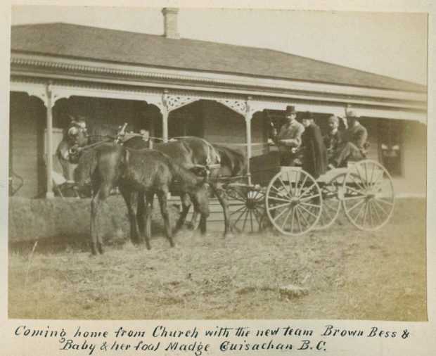 Photo en noir et blanc d’un cheval et d’un chariot avec quatre personnes devant une maison.