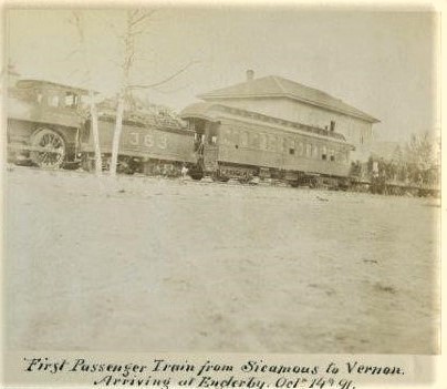 Photo en noir et blanc d’un train, avec la locomotive, une voiture de passagers et un édifice en arrière-plan.