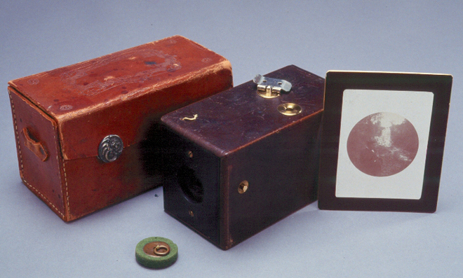 Premier appareil photo Kodak avec son étui et une photo encadrée.