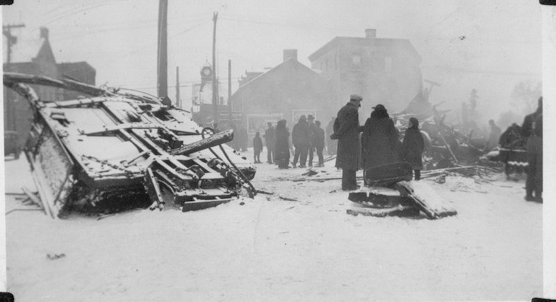 Photographie des décombres de la troisième voiture du train local de la vallée de l’Outaouais, à Almonte; on voit des gens qui marchent dans la ville, 1942