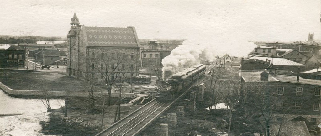 Photographie montrant un train circulant sur la voie ferrée et l’hôtel de ville d’Almonte à l’arrière-plan, années 1950