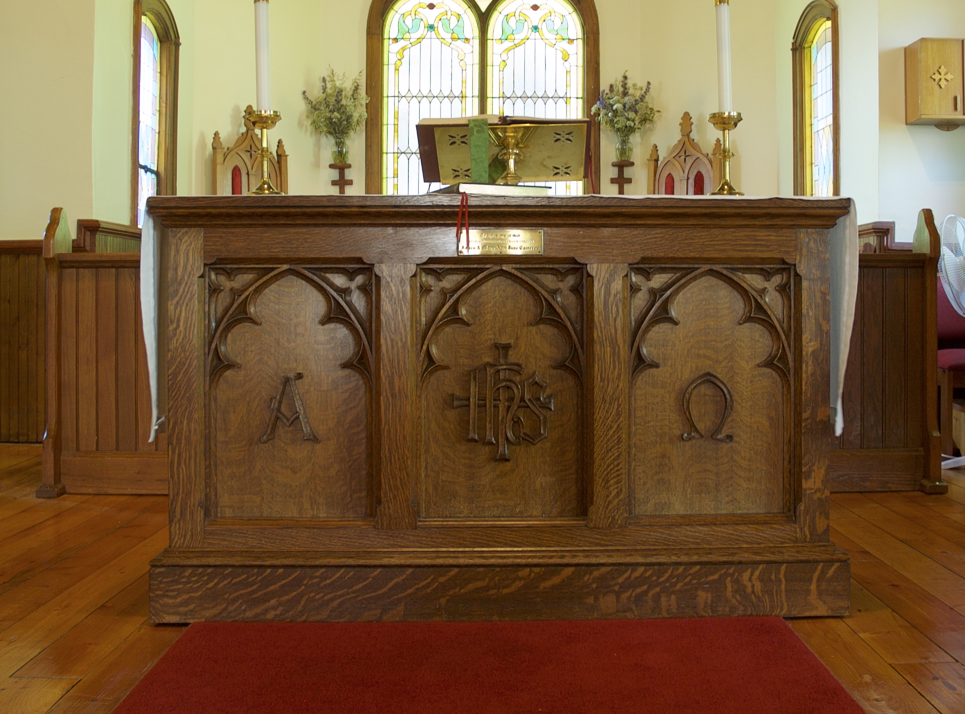 Table de communion ou autel en chêne. Sur le devant, trois panneaux sont sculptés dans le bois. Le panneau de gauche porte le symbole A pour 