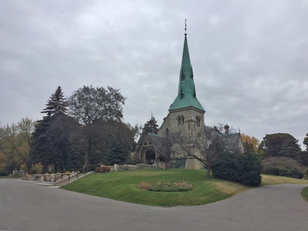 Une photographie de l'église anglicane St. James 'the Less' à Toronto, en Ontario. L'église en pierre a un grand clocher en bronze qui a vieilli en vert. 