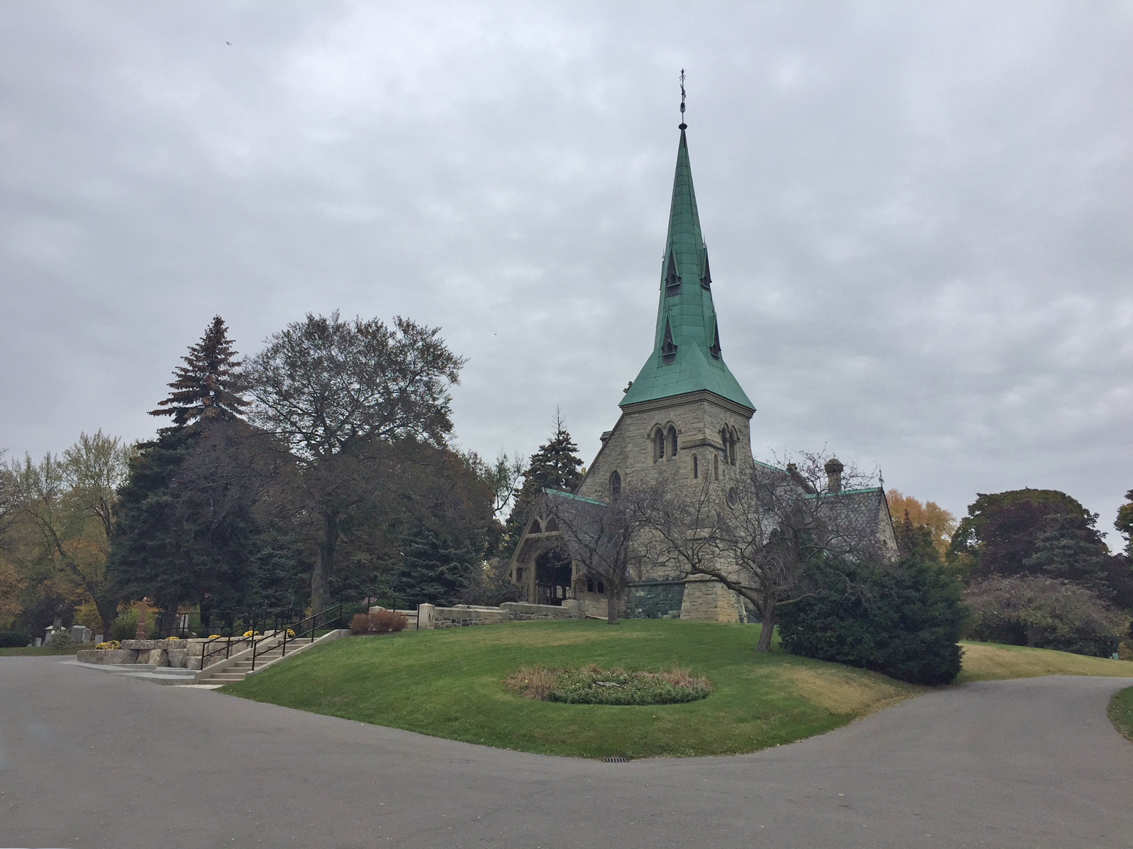 Une photographie de l'église anglicane St. James 'the Less' à Toronto, en Ontario. L'église en pierre a un grand clocher en bronze qui a vieilli en vert. 