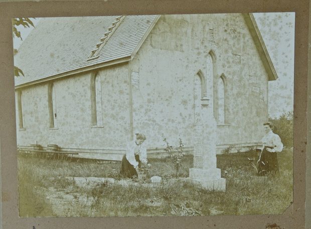 Photographie en noir et blanc de deux femmes à l'arrière de St. James s'occupant d'une tombe, vers 1880. 