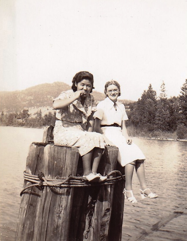 Photo en noir et blanc représentant deux jeunes femmes assises sur des pieux plantés dans un lac.