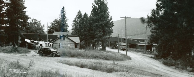 Photo en noir et blanc d’une vieille voiture devant une maison de bois.