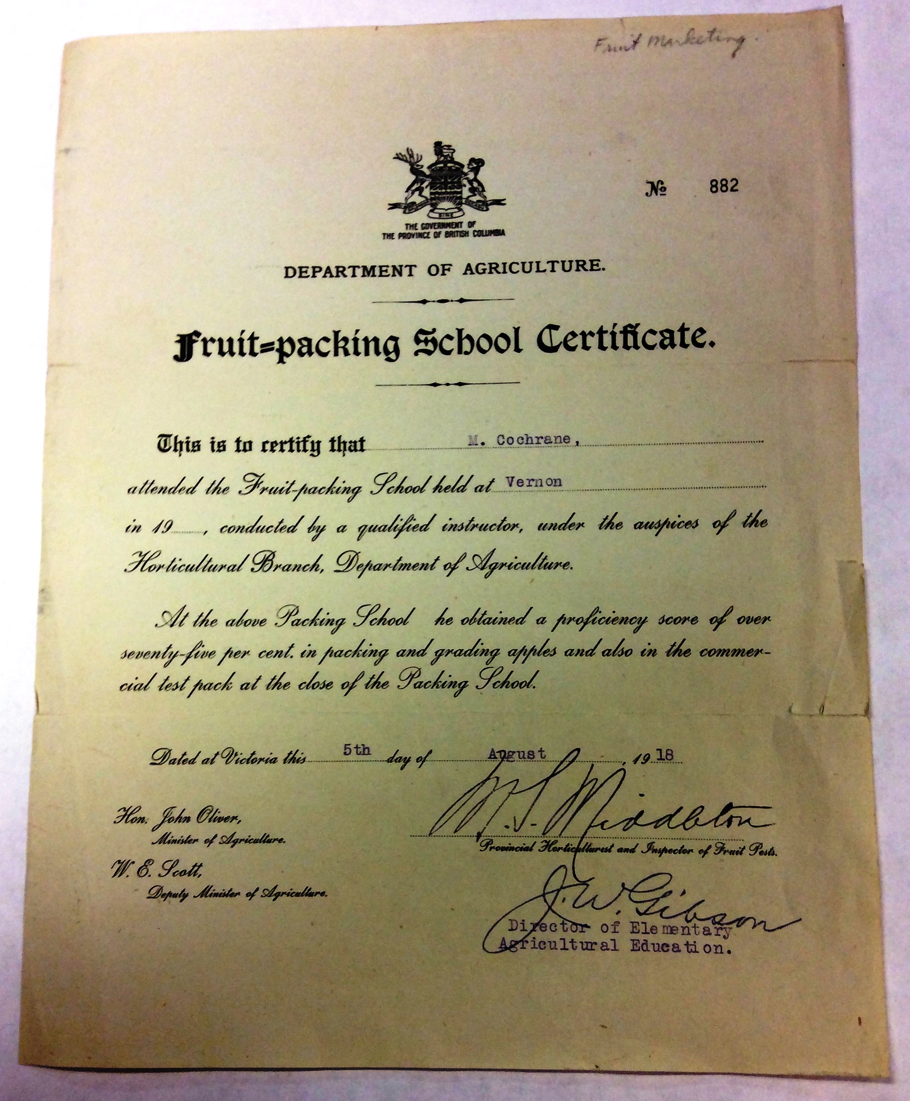 Photo sépia d’un certificat portant le numéro 882 et la mention : « The Government of the Province of British Columbia, Department of Agriculture Fruit Packing School Certificate » (Gouvernement de Colombie-Britannique, Ministère de l’Agriculture, Certificat d’apprentissage de la mise en caisse), établi à Victoria le 5 août 1918 et signé (dans l’angle inférieur droit) par M. J. Middleton, Horticulteur et inspecteur provincial des parasites des fruits, et par J. W. Gibson, Directeur de l’enseignement agricole élémentaire. Signatures imprimées (dans   l’angle inférieur gauche) de l’Honorable John Oliver, Ministre de l’Agriculture et W. E. Scott, Sous-ministre de l’Agriculture.
