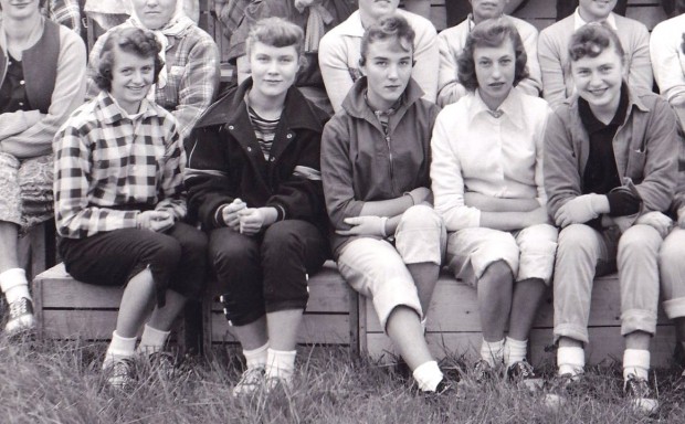 Segment d’une photo en noir et blanc montrant cinq jeunes femmes assises dehors sur des caisses de bois.