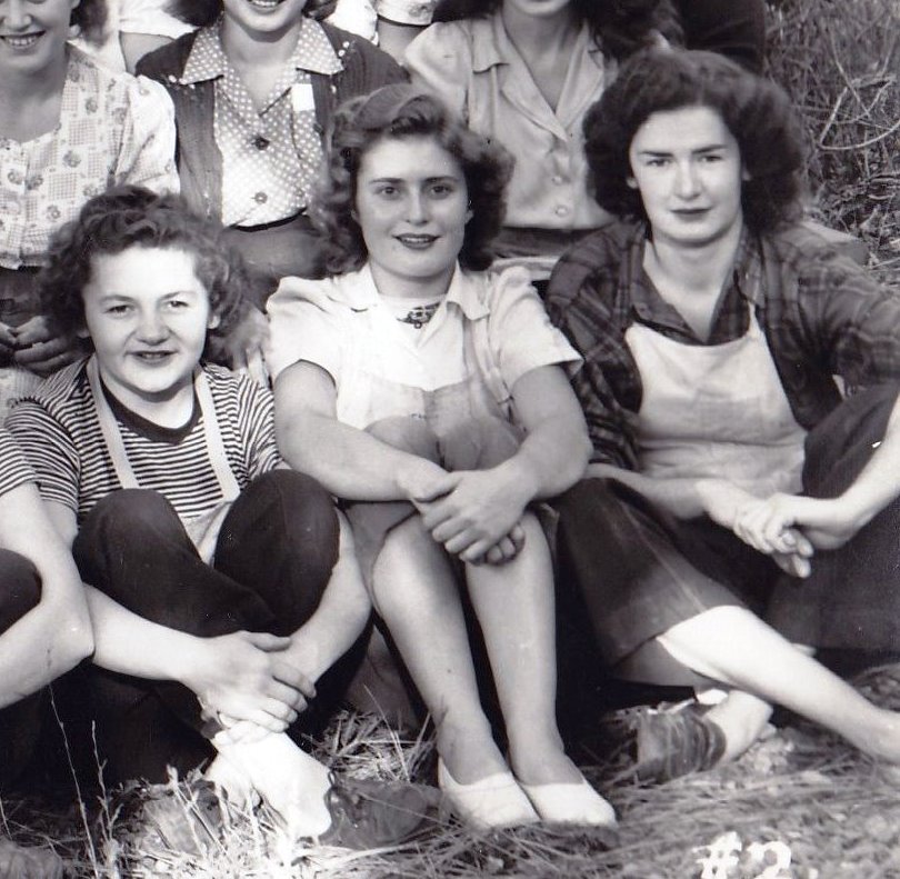 Segment d’une photo en noir et blanc représentant trois jeunes femmes assises dans l’herbe.