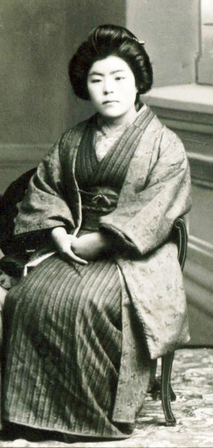 Photo en noir et blanc d’une jeune femme assise. Elle porte un costume d’apparat japonais traditionnel.
