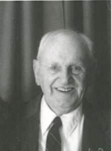 Photo en noir et blanc de Bill Parsons souriant, portant un complet.