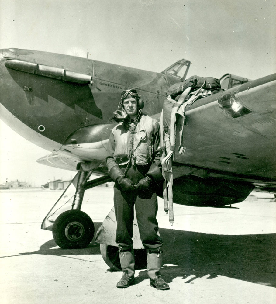 Photo en noir et blanc de Lamont Parsons, dans sa combinaison de vol, debout à côté de son avion de chasse Hawker Hurricane, un sac de parachute posé sur l’aile.