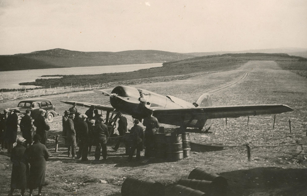 Photographie en noir et blanc d’une petite foule rassemblée autour de l’avion, le Dorothy, sécurisé sur la piste d’atterrissage.