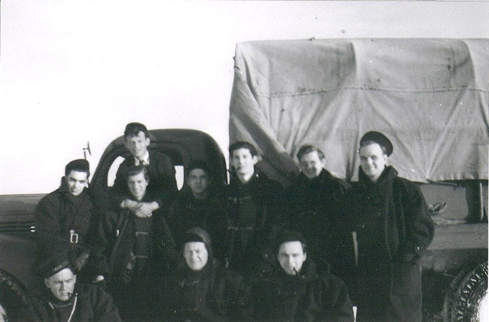 Photographie en noir et blanc de dix officiers de la Marine posant devant un camion couvert de la Marine.