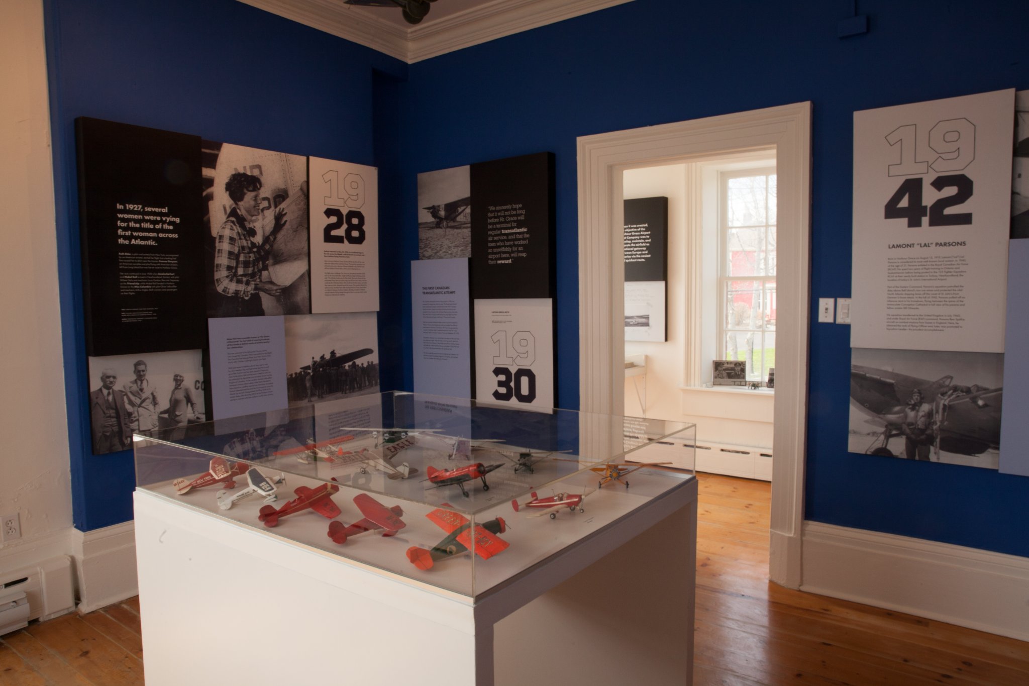 Photographie en couleurs d’un espace d’exposition où des scénarimages sont affichés au mur et où une vitrine présente 12 petits modèles réduits d’avions.