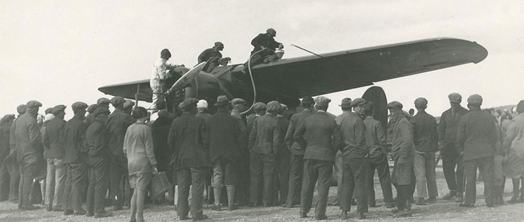 Photo en noir et blanc de trois personnes se trouvant sur les ailes d’un avion, lors du ravitaillement. Une foule nombreuse se tient autour de l’avion, dos à l’appareil-photo.