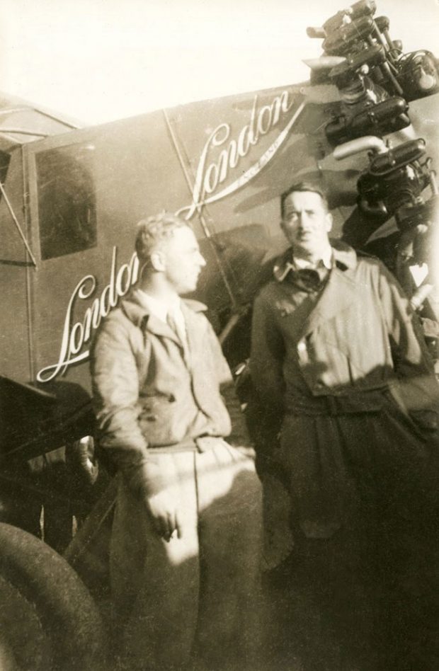 Photographie en noir et blanc de James Medcalf et Terrence Tully en uniforme d’aviateur, debout devant l’avion Sir John Carling entre le poste de pilotage et l’hélice.