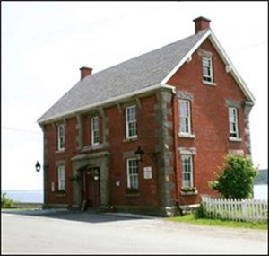 Photo en couleurs d’un bâtiment historique en briques, sur le bord de la route. 