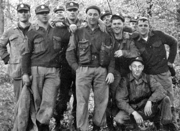 Groupe de dix soldats posent pour une photo dans un endroit boisé 