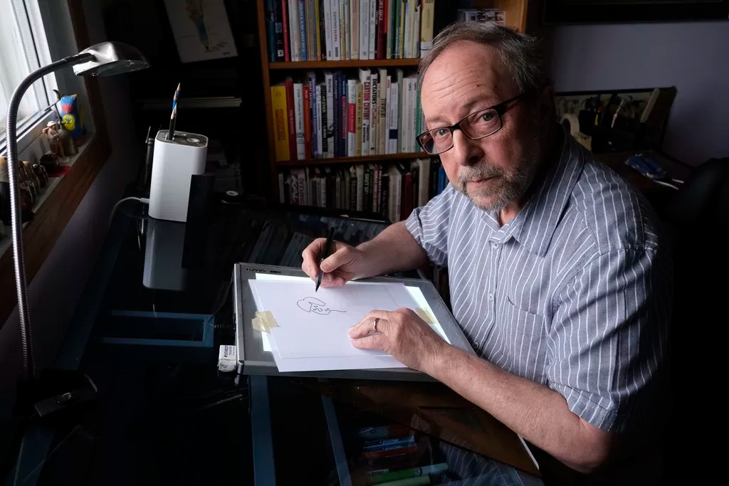 Photo de Bado, assis à sa table à dessin.