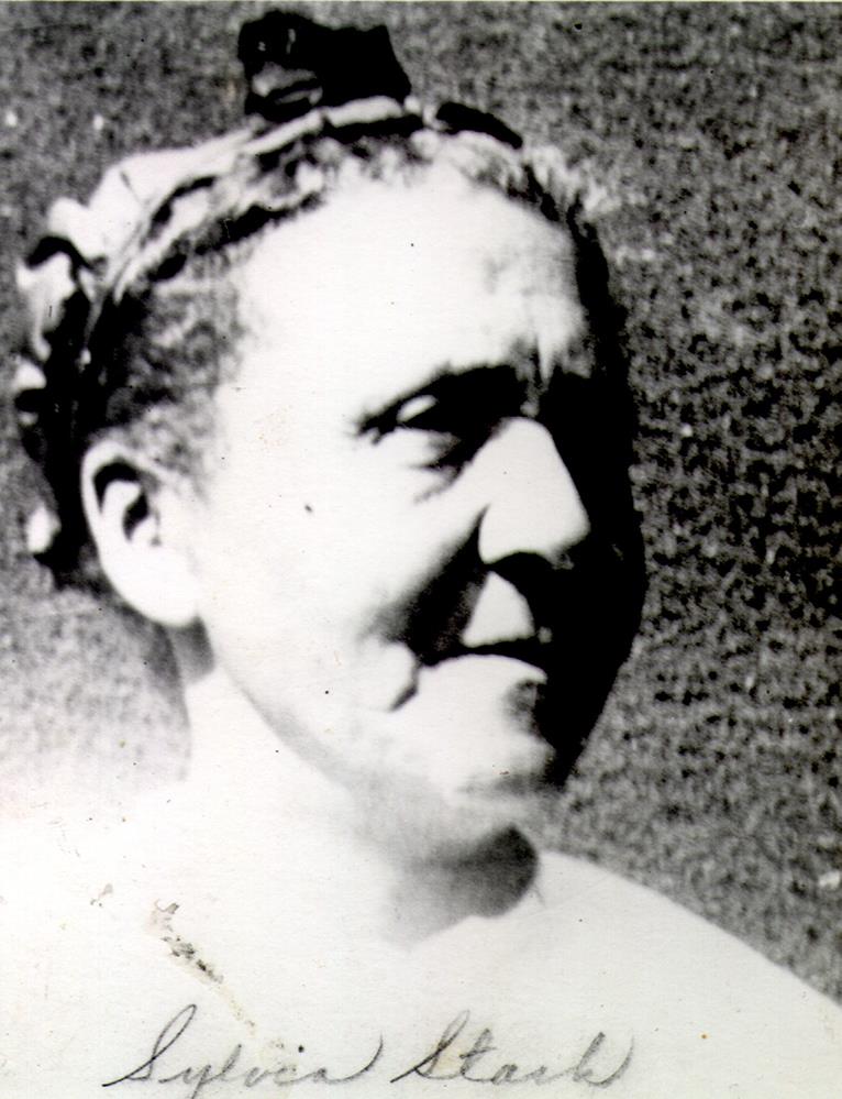 portrait en noir et blanc d’une femme d’âge moyen, cheveux tirés vers l’arrière et portant un bandeau décoratif