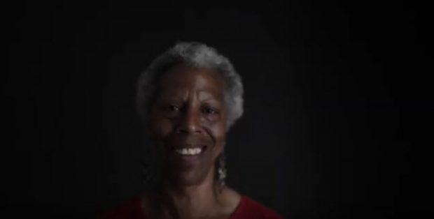 portrait d’une femme mince et âgée arborant une coiffure afro courte, souriante, dans un studio, fond noir